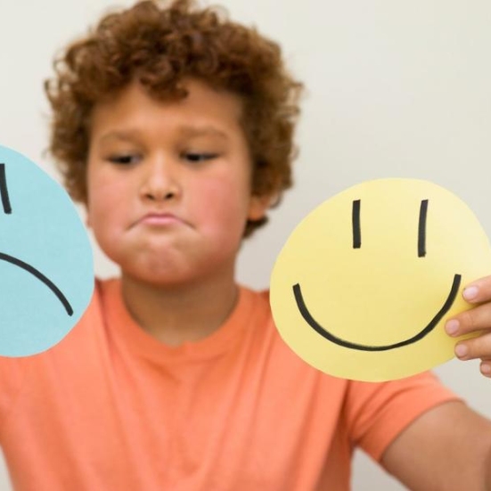 Billede af dreng, der holder en glad og en sur smiley op foran sig