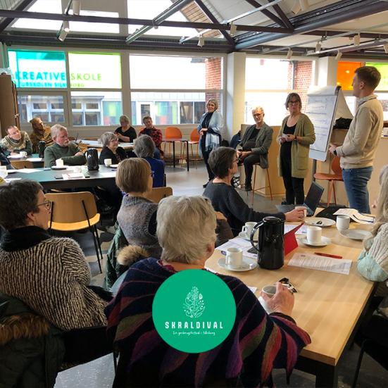 En gruppe mennesker, der sidder og drikker kaffe og hører et oplæg