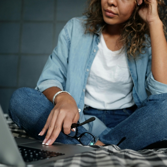 kvinde i skrædderstilling arbejder på pc. læsebriller i hånden