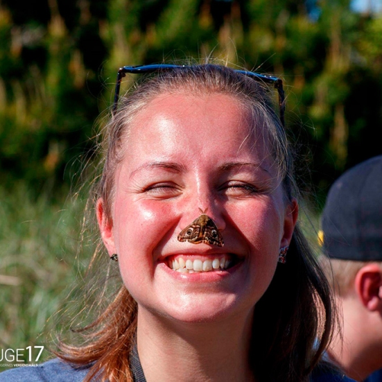 En smilende kvinde med en sommerfugl siddende på næsen.