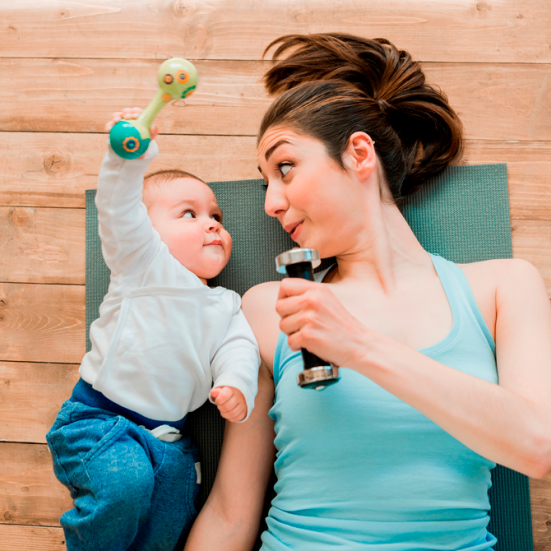 Baby og kvinde ligger på jorden på en yogamåtte med træningsudstyr. De kigger på hinanden