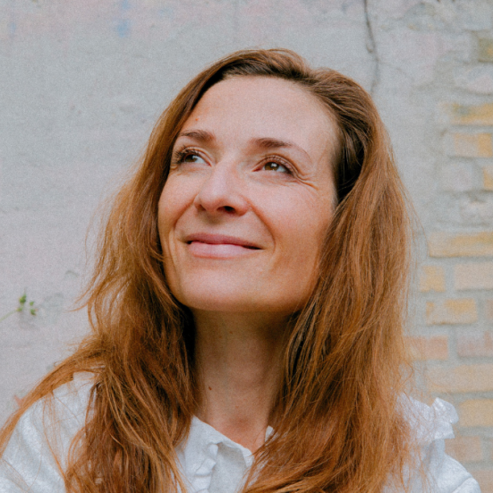 Iben Maria Zeuthen foran en murstensvæg. Hun kigger op og smiler. 