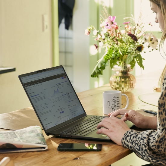 kvinde set fra siden, arbejder på pc, i baggrunden kaffekop og blomsterbuket