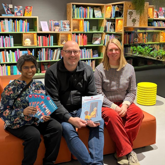 Billede af de tre mennesker, der afholder Ordblindecaféen. De sidder i en orange sofa i Outdoorbiblioteket, Silkeborg Bibliotek. 