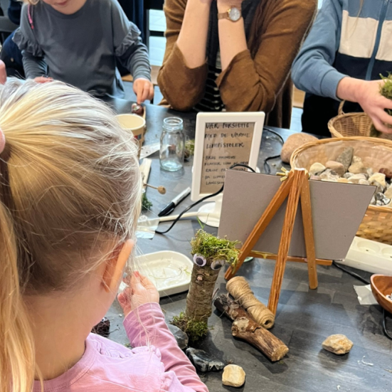 Pige med ryggen til, der sidder ved et bord og laver krea-aktiviteter med andre børn. 