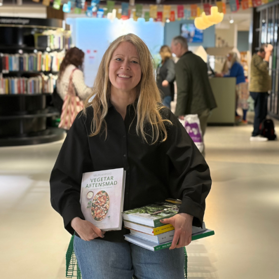 Formidler sidder ned med en stak vegetariske kogebøger midt i biblioteksrummet