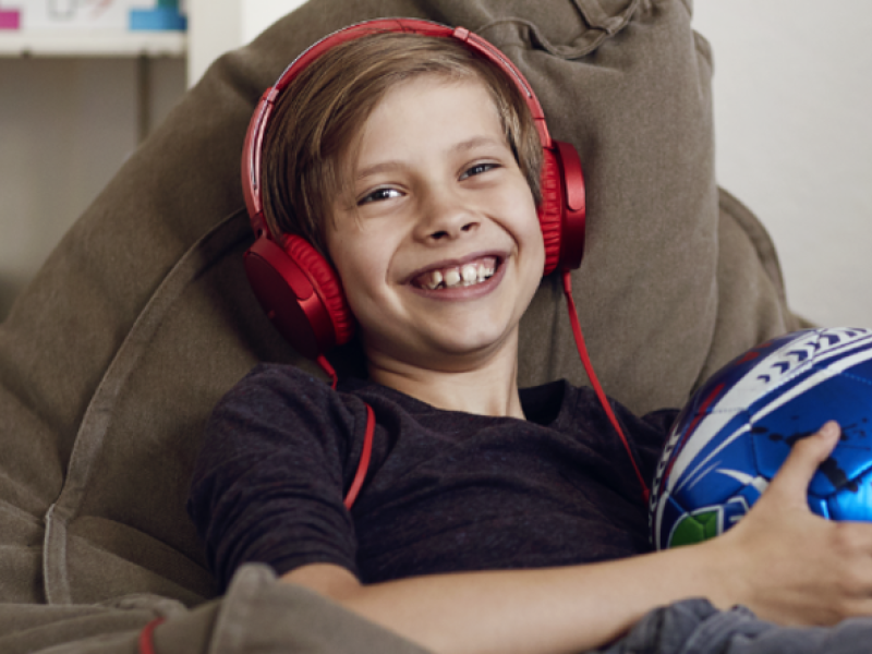 Dreng sidder med røde hørebøffer på og smiler