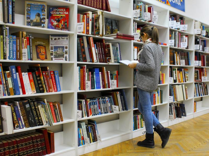 Kvinde står og kigger i bøger foran stor bogreol