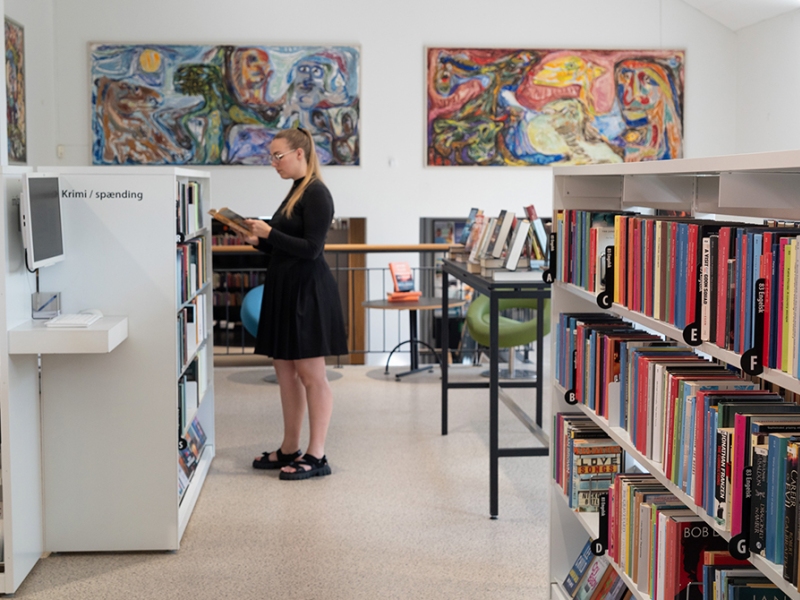 Kvinde står i biblioteksrummet og kigger i en bog