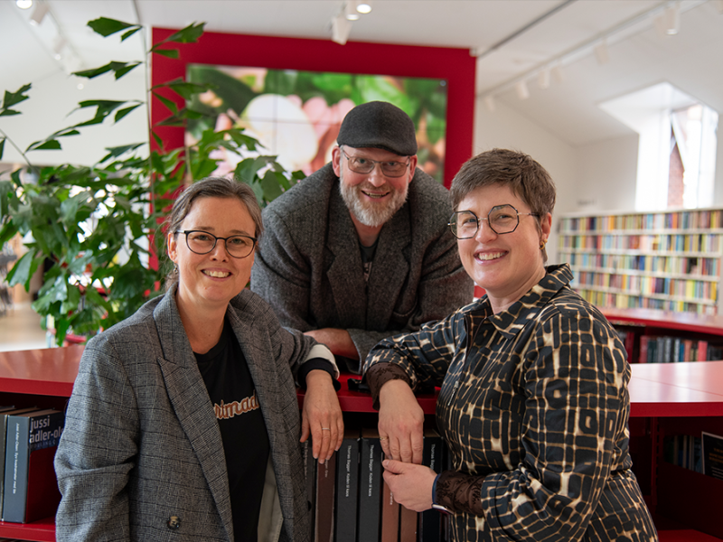Tre mennesker står samlet i et biblioteksrum