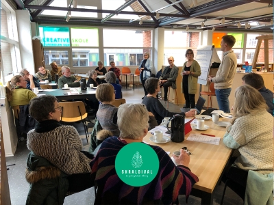 En gruppe mennesker, der sidder og drikker kaffe og hører et oplæg