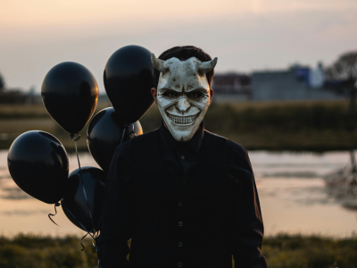 Mand med djævlemaske og sorte balloner.