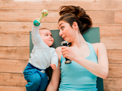 Baby og kvinde ligger på jorden på en yogamåtte med træningsudstyr. De kigger på hinanden