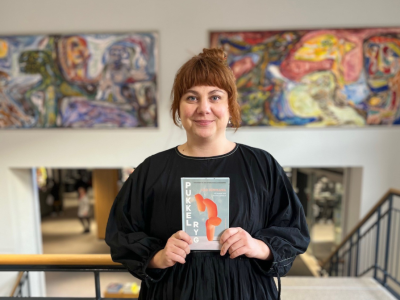 Formidler Emma i biblioteksrummet foran Asger Jorn malerierne med romanen "Pukkelryg" i hænderne