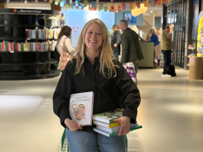 Formidler sidder ned med en stak vegetariske kogebøger midt i biblioteksrummet