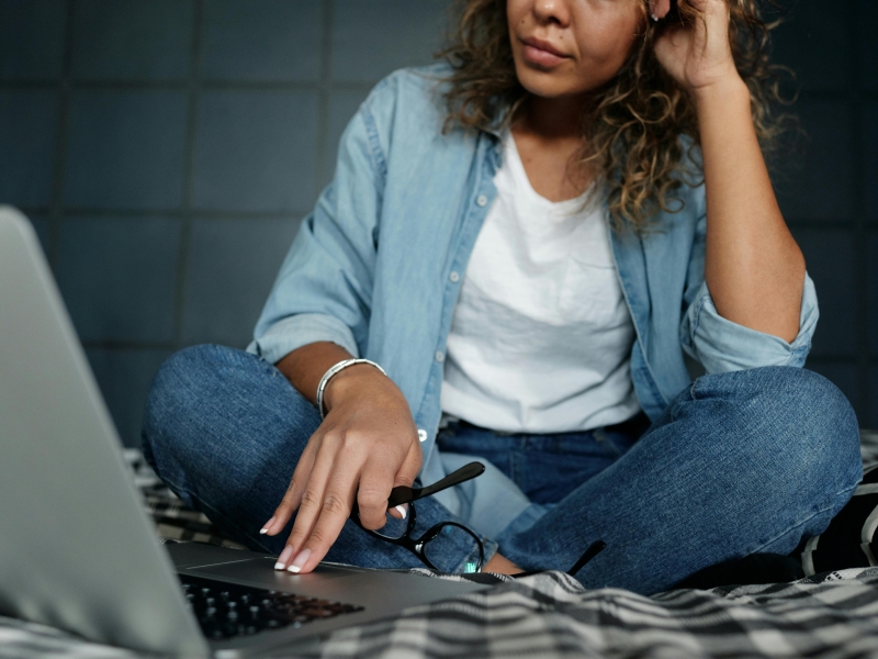 kvinde i skrædderstilling arbejder på pc. læsebriller i hånden