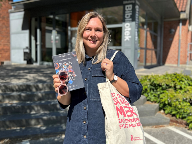 Formidler Kirstine foran Silkeborg Bibliotek med en mulepose og bog