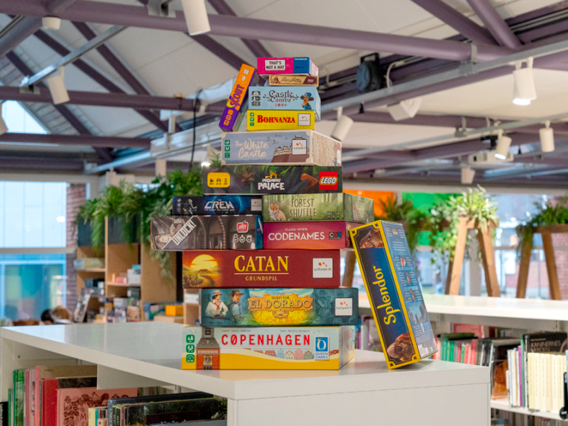 En stak af brætspil stående på en bogreol på Silkeborg Bibliotek. 