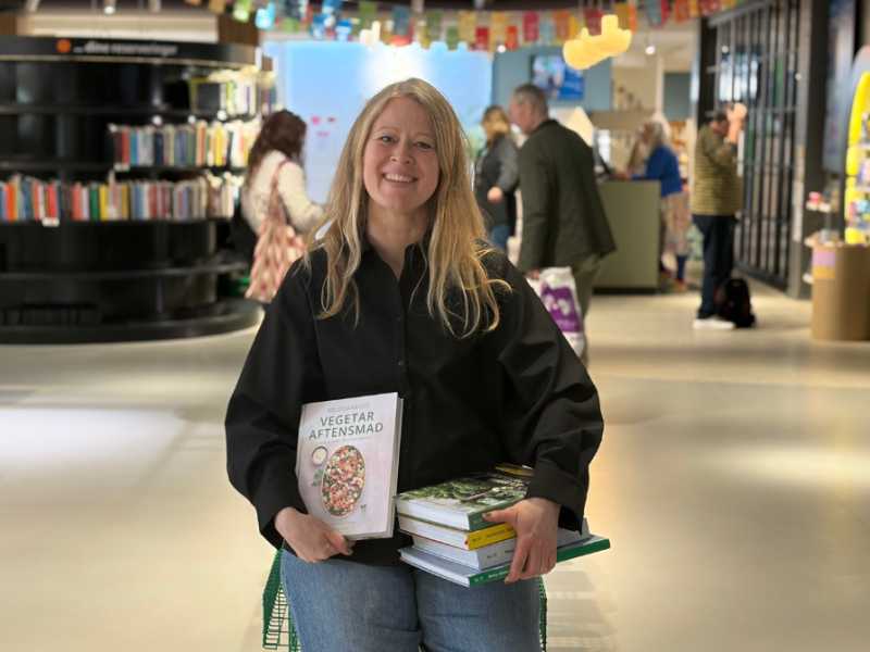 Formidler sidder ned med en stak vegetariske kogebøger midt i biblioteksrummet