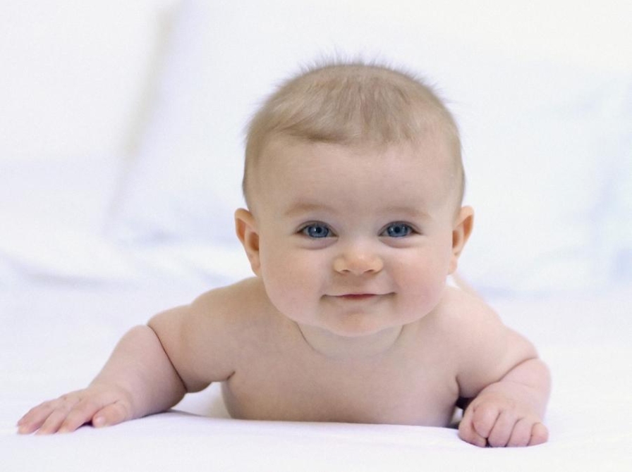 Baby ligger på maven og kigger smilende op