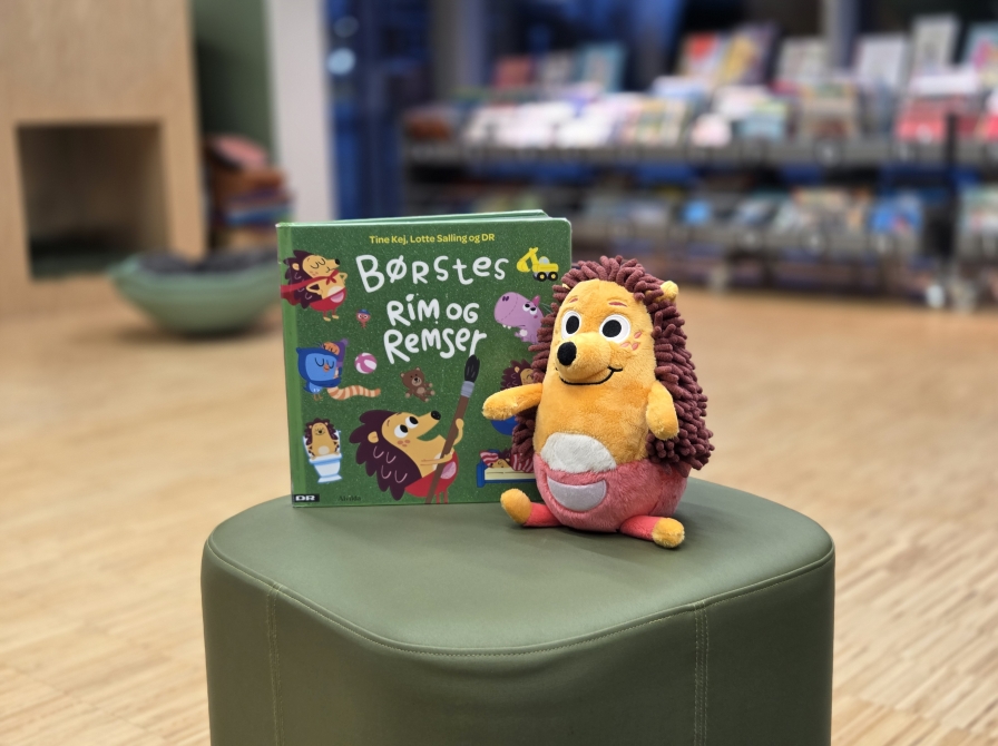 Børste-bamsen og bogen "Børstes rim og remser" på en grøn puf på Kjellerup Bibliotek