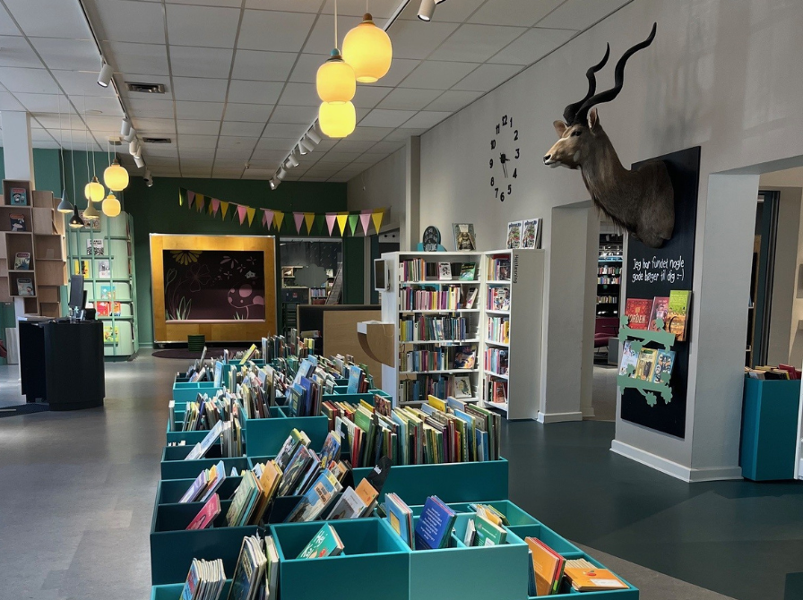 Børnebiblioteket på Silkeborg Bibliotek. Kasser med bøger, et udstoppet Kudu-hoved på væggen og en flagranke i baggrunden. 