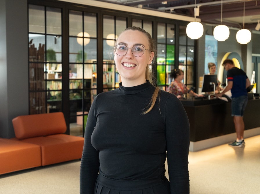 Kvinde med mørk trøje og briller på et bibliotek