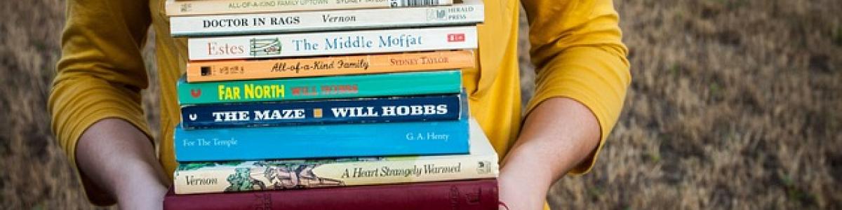 kvinde i gul trøje holder en stak bøger