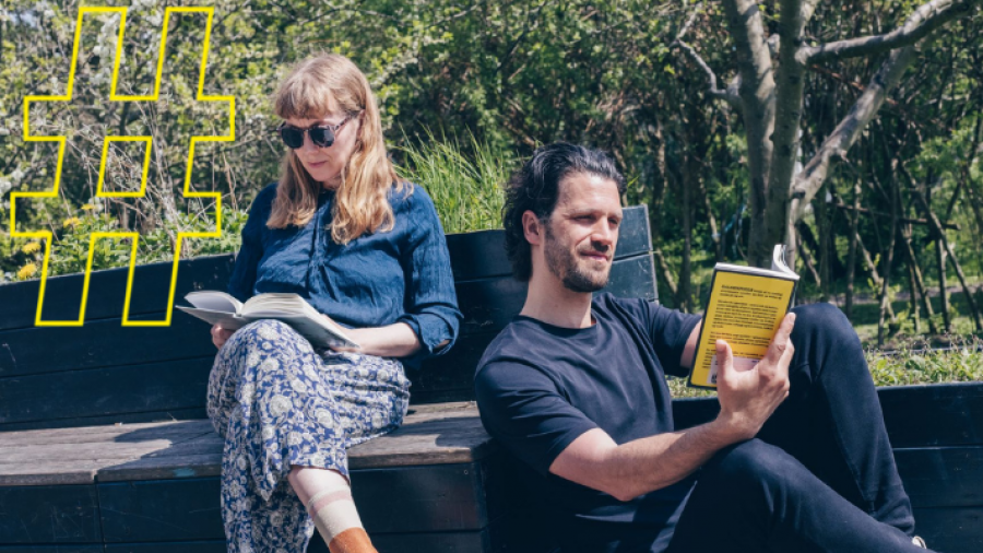 En mand og en kvinde sidder på en bænk i skoven og læser sammen