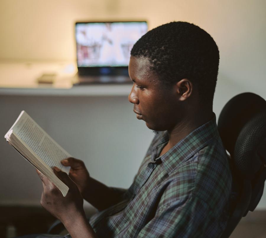 Mand der læser en bog med en computer i baggrunden
