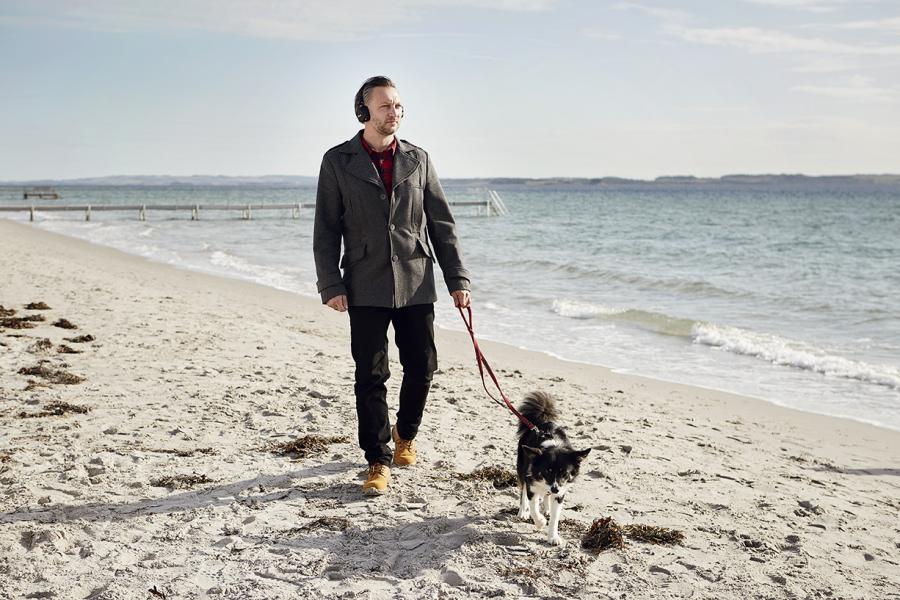 Mand går med hund på strand med hørebøffer på