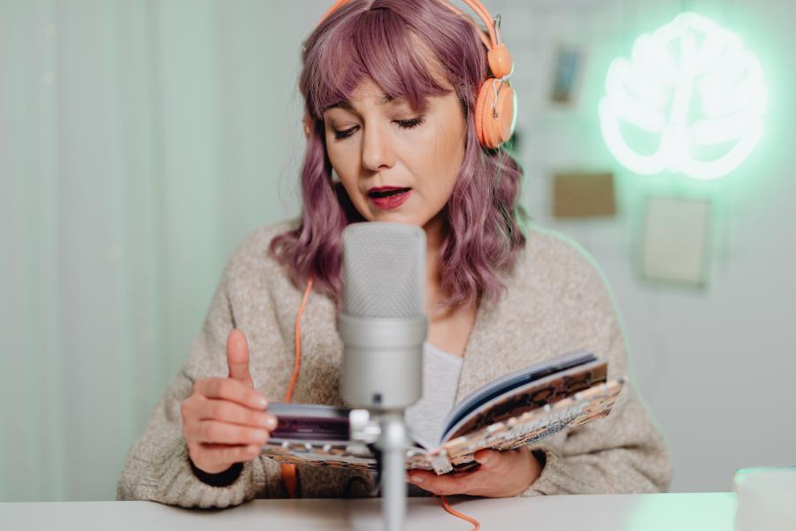 Kvinde med orange headphones, mikrofon og bog