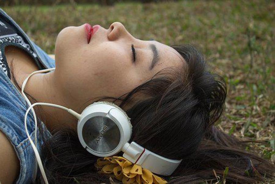 Ung kvinde ligger i græsset med høretelefoner på