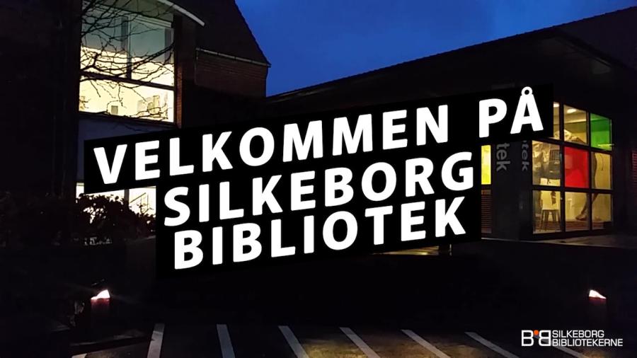 Silkeborg bibliotek i mørke med lys fra vinduerne. På billedet teksten "velkommen til Silkeborg Bibliotekerne"